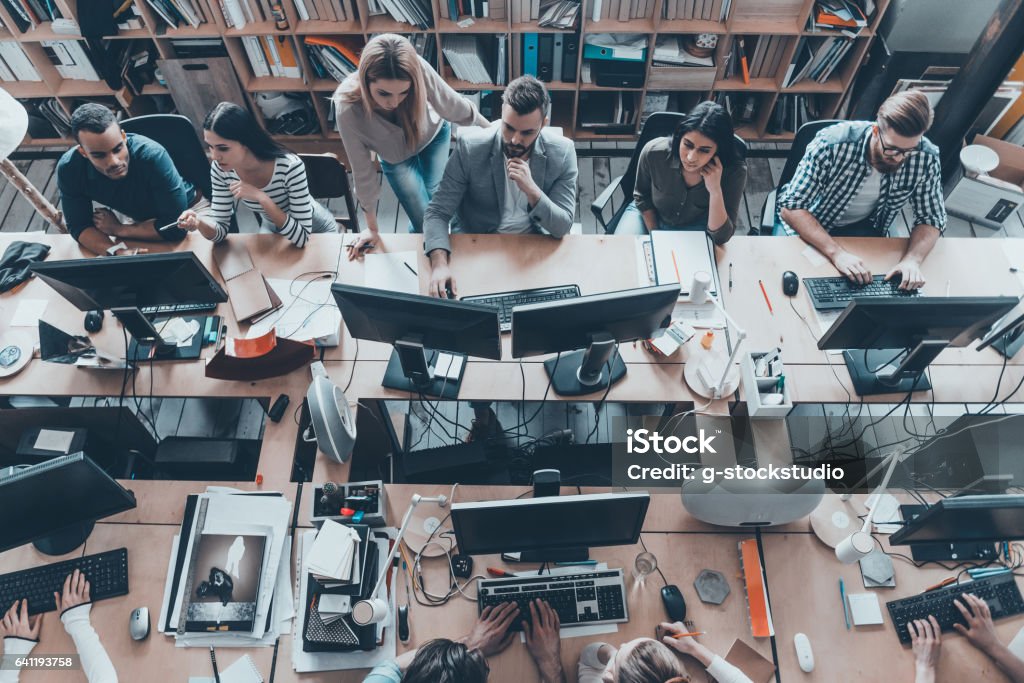 Busy working in office. Top view of group of young business people in smart casual wear working together while sitting at the large office desk Modern Stock Photo