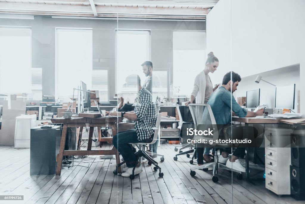 Successful professionals. Group of business people using computers and communicating while working behind the glass wall in the creative office Office Stock Photo