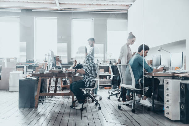 Successful professionals. Group of business people using computers and communicating while working behind the glass wall in the creative office design studio stock pictures, royalty-free photos & images