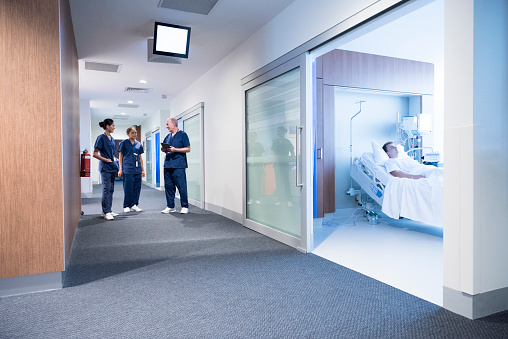 Three doctors discussing with young man recovering in hospital room