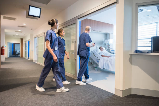 Medical team entering hospital ward where male patient is lying in bed Male doctor and two female nurses wearing uniform and walking through doorway hospital room stock pictures, royalty-free photos & images