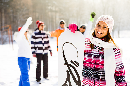 Group of young people with snowboards on winter holiday, Portrait of smiling woman with snowboard with friends in background.