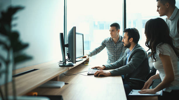 Group of IT experts in their office. Closeup side view of group of young IT experts completing a task, a part of their daily routine at IT company. There are three men and a woman. outsourcing stock pictures, royalty-free photos & images