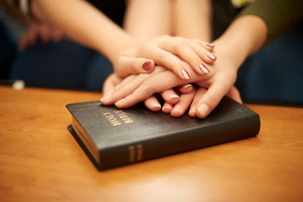 prayer group teen hands a group of four teenage girls sit at home and place their hands on the bible as they prayer together . bible study group of people small group of people stock pictures, royalty-free photos & images