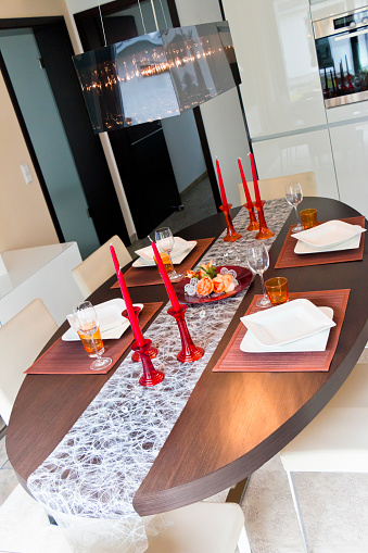 Festive modern dining table with dishes, glasses, cadles and decoration, integrated into a modern kitchen in high gloss finish.