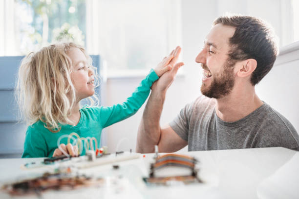 Dad Teaching Daughter Electrical Engineering A cute young girl, 4-5 years old, works on an educational circuit board, learning the basics of electrical engineering to give her an edge in the world of women in science and technology. Her father teaches her, giving her guidance as she learns. encouragement stock pictures, royalty-free photos & images