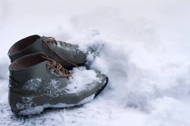 side view close up of a grey pair of vintage brown leather shoes covered in snow in winter time