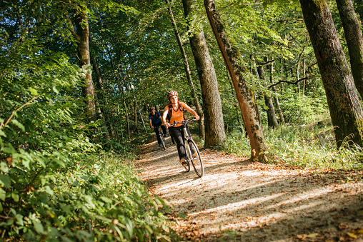 Young couple is cycling on footpath in nature. Sun is shining and mountains are in the back.