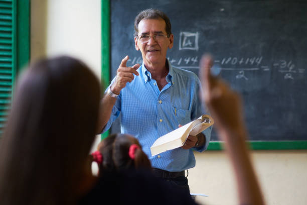 девушка поднимая руку задавая вопрос учителю в школе - professor teacher female blackboard стоковые фото и изображения