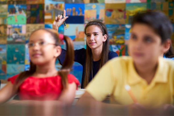 Smart Girl Raising Hand And Asking Question At School Young people and education. Group of students in class at school during lesson. Girl raising hand and asking question to professor junior high stock pictures, royalty-free photos & images