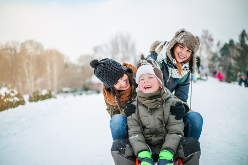 Gay (lesbian) parents and son enjoy in sledding on snow. Two young mothers and son