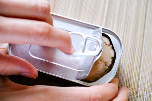 Woman hand opening tin can with cod liver