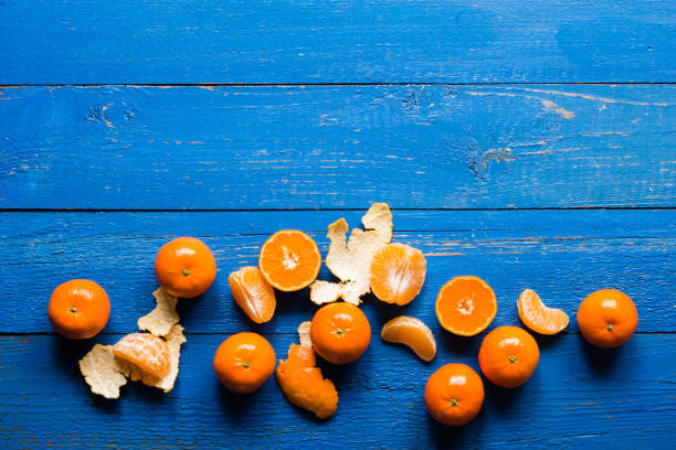 whole, cutted and pilled mandarins on a blue painted wooden background - pilled imagens e fotografias de stock