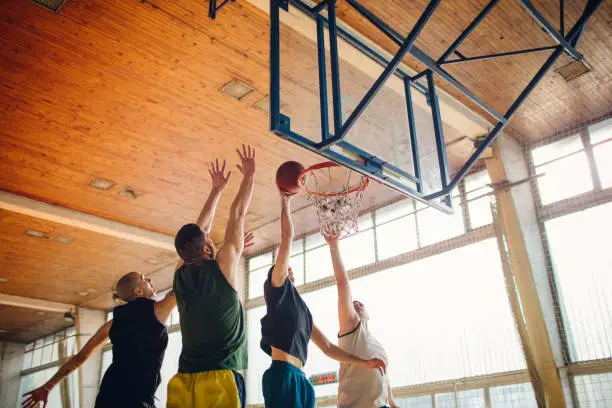 Group of friends playing basketball indoors. One player throwing ball in net