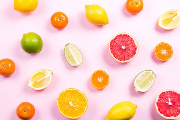 Photo of Several kinds of whole and cut citrus on a pink background