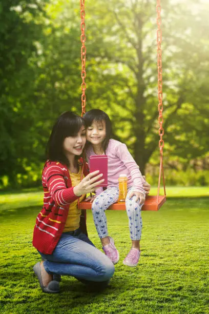 Portrait of young mother and cute child taking selfie picture while sitting on the swing