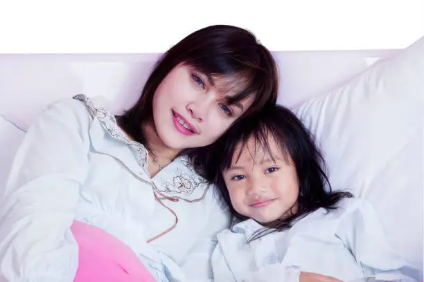 Portrait of young mother and daughter leaning on the bed while looking at the camera
