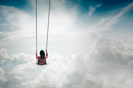 Image of young woman enjoying her time while swinging above the clouds