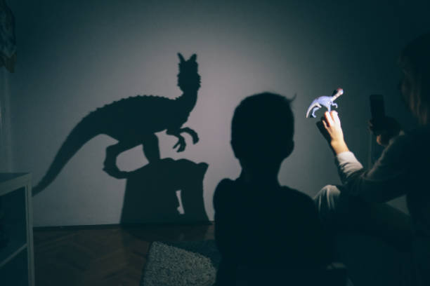 Mom's shadow puppet show Little boy and his mother are playing with shadow puppets on the wall by using dinosaur toys dinosaur photos stock pictures, royalty-free photos & images