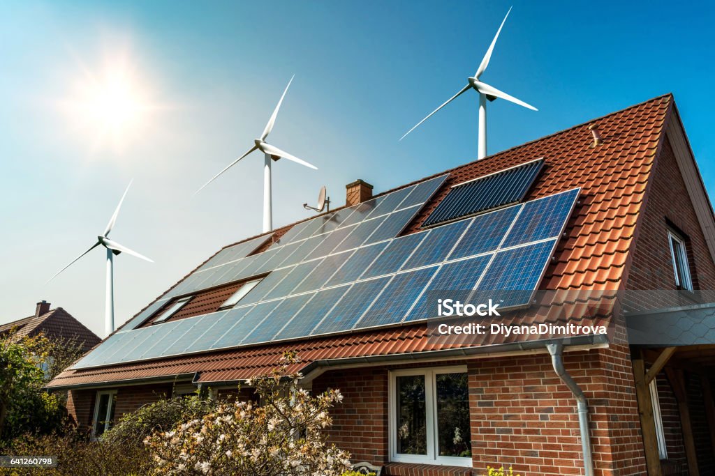 Solar panel on a roof and wind turbins arround Solar panel on a roof of a house and wind turbins arround - concept of sustainable resources Solar Panel Stock Photo