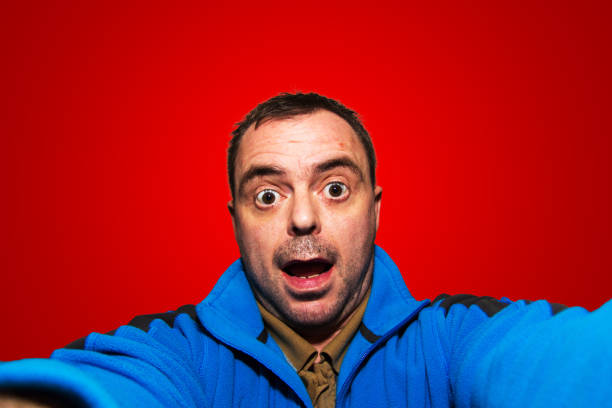 Man talking selfie pulling funny face on red background stock photo