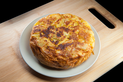 Spanish potatoe omelet in dish over wood surface and black background.