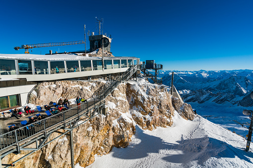 Garmisch-Partenkirchen, Bayern (Bavaria) Germany - buildings at the summit of the Zugspitze which also forms part of the border between Germany and Austria. People can be seen enjoying the sunshine on a deck and inside buildings that form the Austrian part of the complex.