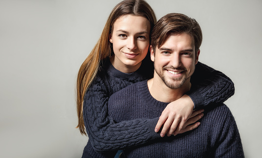 Portrait of smiling young couple wearing navy blue sweaters against gray background