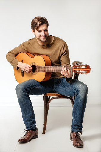 Full length portrait of smiling man playing guitar while sitting on chair against white background