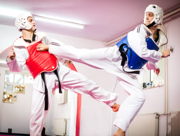 Two taekwondo fighters compete and practice high kicks with protective equipment Taekwondo training in sport hall with tatami. Taekwondo is equally popular sport among girls and boys, young men and women. Sport develops physique and strength on lower and upper limbs equally. Professional taekwondo players practice with protective sportswear taekwondo stock pictures, royalty-free photos & images