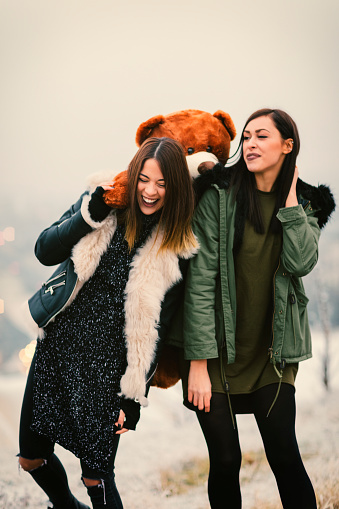 Happy Young Women Having Fun Outdoors on the top of the hill. Hodling   teddy bear with the city in fog in background