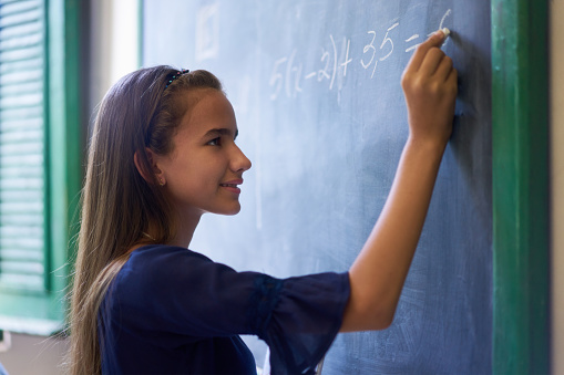 Young people and education. Group of hispanic students in class at school during lesson. Portrait of happy girl doing math exercise at blackboard