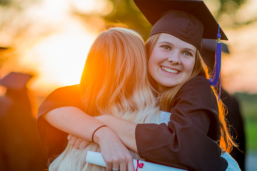 Two high school graduates are hugging after the graduation ceremony.