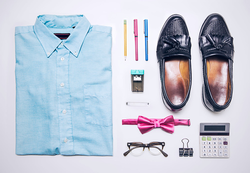 An overhead view of a collared shirt, bow tie, granny glasses, calculator, and other accessories of a stereotypical nerd character.