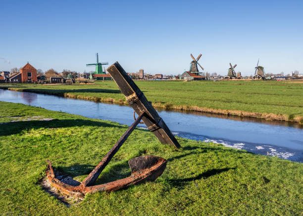 Old rusty anchor on green grass and windmills background landscape in Zaanse Schans, Amsterdam stock photo