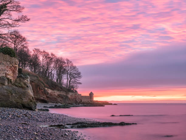 Colorful sunrise with burning sky over rocky beach with ruins of old watch tower near Kirkcaldy, Scotland stock photo