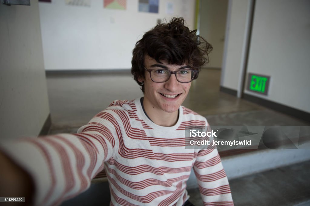 Teen Boy With Glasses Taking Selfie Smiling A teen boy with glasses taking a selfie smiling in stripped short. Selfie Stock Photo