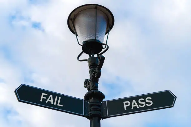 Street lighting pole with two opposite directional arrows over blue cloudy background. Fail versus Pass concept.