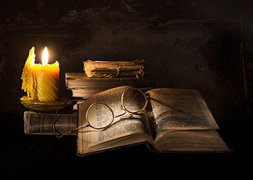 Still life with old books, old glasses and wax candle.Wax candle is drip.Lighted with flashlight.