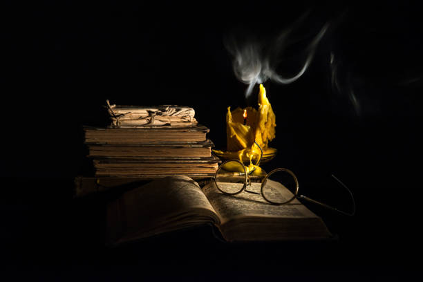 Still life with old books, old glasses and wax candle.Wax candle is drip. The candle is blown and steaming. Lighted with flashlight.