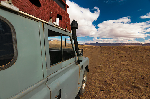 Side of an four by four oldtimer off-road vehicle driving off- road in a desert in Morocco. The vehicle is fully equipped with roof rack  and other off- road items.