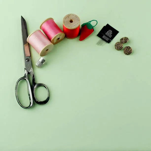 Arrangement of thread, needles, scissors, on light green background with space for copy