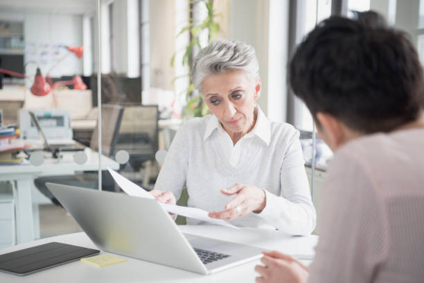 istock Two businesswomen using laptop, senior woman holding document 641311032