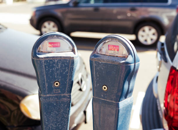 Parking meter showing expired time, with cars seen violating the parking order in background.