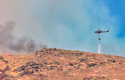 Firefighting water tanker helicopter dropping water on a desert wildfire.