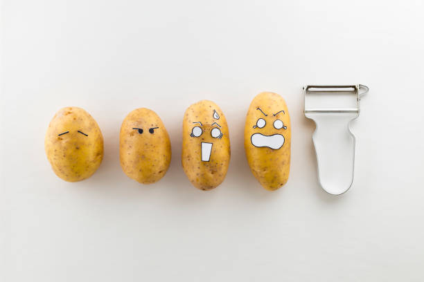 Fresh potatoes with cartoon style faces laying on white surface are scared from a peeler