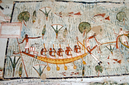 Ancient Egyptian mural on the wall of a tomb showing five oarsmen operating a rowing boat across a sacred lake awash with fish and lotus plants.  Historic painting in the tomb of Amenemonet a priest from the Ramesside Period, West Bank of the Nile at Luxor, Egypt.