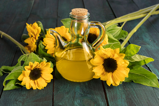 A photo of a pitcher of sunflower oil on a wooden board with flowers and a place for text