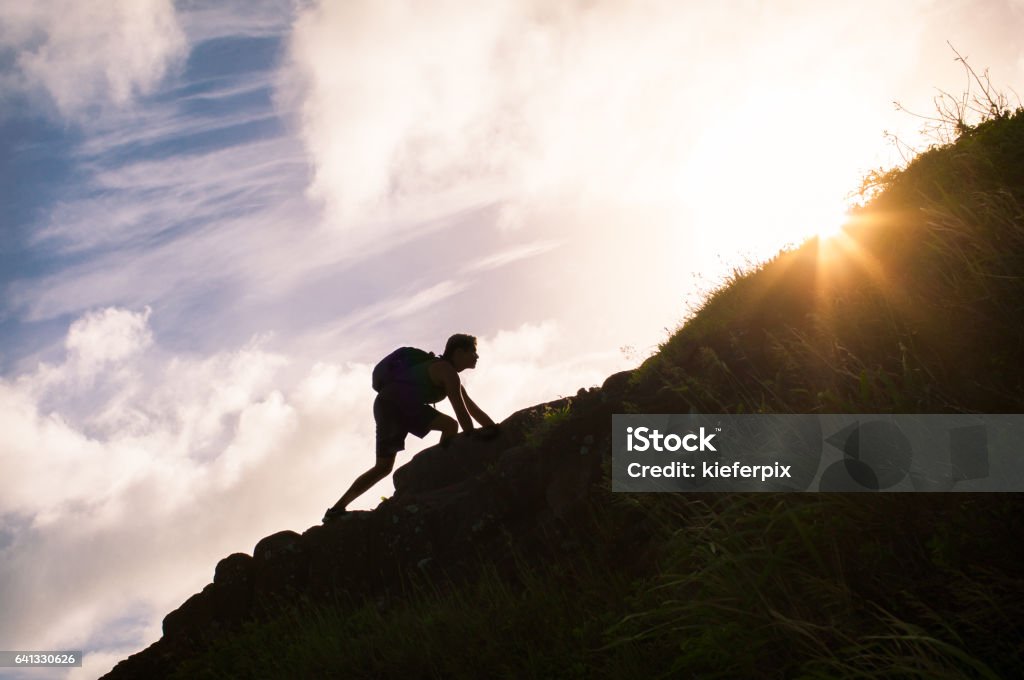 Young man climbing up a mountain. Self improvement and life goals concept. Conquering Adversity Stock Photo