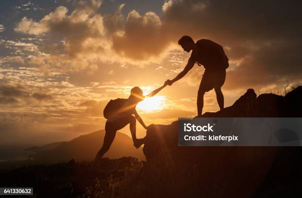 Male And Female Hikers Climbing Up Mountain Cliff And One Of Them Giving Helping Hand Stock Photo - Download Image Now